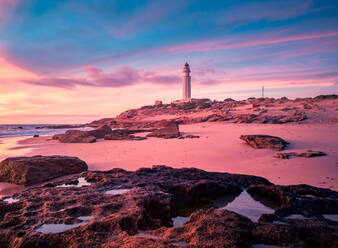 Herrlicher Blick auf den Leuchtturm auf einem Hügel in der Nähe des Meeres vor einem farbenfrohen Himmel bei Sonnenuntergang in Cádiz - ADSF21070