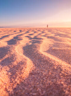 Fernansicht einer nicht erkennbaren Person, die am Sandstrand spazieren geht, vor dem Hintergrund des Sonnenuntergangs in Cadiz - ADSF21071