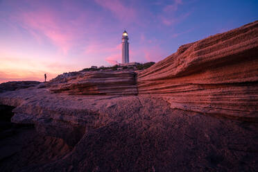 Herrlicher Blick auf den Leuchtturm auf einem Hügel in der Nähe des Meeres vor einem farbenfrohen Himmel bei Sonnenuntergang in Cádiz - ADSF21072