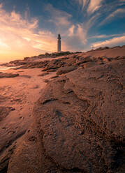 Herrlicher Blick auf den Leuchtturm auf einem Hügel in der Nähe des Meeres vor einem farbenfrohen Himmel bei Sonnenuntergang in Cádiz - ADSF21074