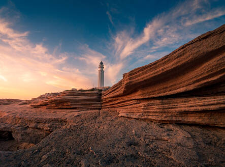 Herrlicher Blick auf den Leuchtturm auf einem Hügel in der Nähe des Meeres vor einem farbenfrohen Himmel bei Sonnenuntergang in Cádiz - ADSF21075