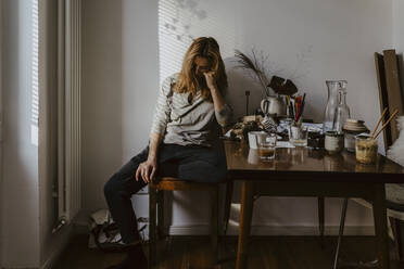 Depressed woman sitting on chair in living room - MASF21910