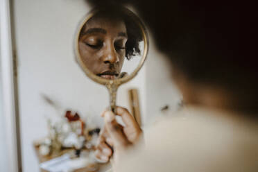 Woman holding mirror with eyes closed at home - MASF21931