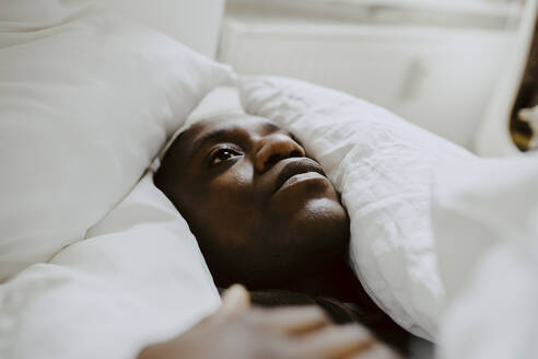 Depressed man lying amidst pillow in bedroom - MASF21948