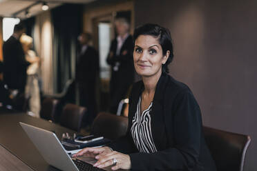 Porträt einer lächelnden Geschäftsfrau, die mit einem Laptop am Konferenztisch im Sitzungssaal sitzt - MASF21984