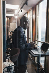 Seitenansicht eines glatzköpfigen männlichen Unternehmers, der einen Laptop im Sitzungssaal benutzt, gesehen durch eine Glaswand - MASF22021