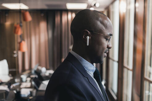 Profilansicht eines glatzköpfigen Geschäftsmannes mit In-Ear-Kopfhörern im Sitzungssaal eines Büros - MASF22022