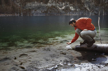 Männlicher Tourist hockt auf einem Baumstamm mit Wasser in der Hand am Kaindy-See - AZF00202