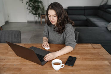 Female entrepreneur working on laptop sitting at table in living room - OGF00916