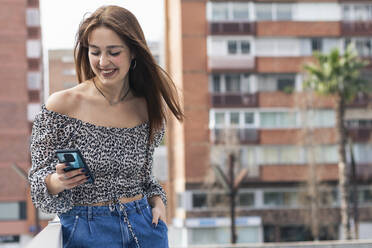 Smiling young woman using mobile phone in city - PNAF00829