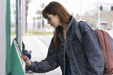 Weiblicher Pendler, der einen Kiosk an einer Straßenbahnhaltestelle benutzt - PNAF00837