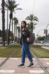 Frau mit Rucksack auf den Gleisen einer Straßenbahnhaltestelle stehend - PNAF00838