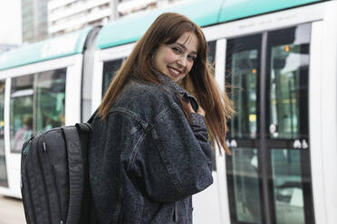 Cheerful young woman standing against train at tram station - PNAF00840