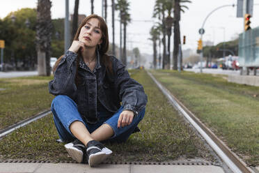 Confident young woman sitting on track at tram station - PNAF00844