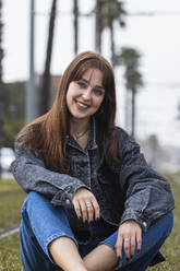 Smiling young woman sitting on track at tram station - PNAF00846