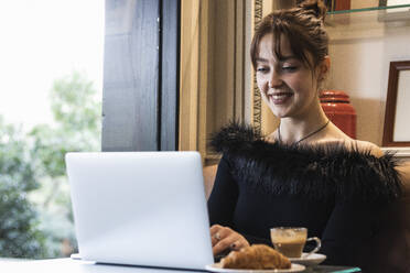 Smiling beautiful businesswoman working on laptop while sitting at cafe - PNAF00859