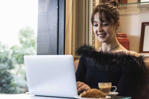 Lächelnde schöne Geschäftsfrau, die im Café sitzend am Laptop arbeitet - PNAF00859