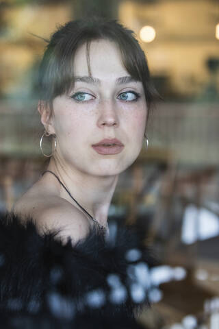 Schöne Frau mit blauen Augen schaut durch ein Fenster in ein Café, lizenzfreies Stockfoto