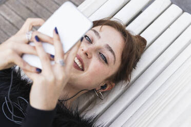 Lächelnde junge Frau, die auf einer Bank liegend im Internet surft - PNAF00878