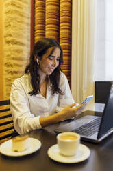 Weibliche Unternehmerin benutzt ihr Smartphone, während sie in einem Café sitzt - JRVF00319