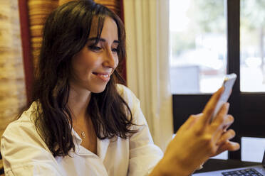 Lächelnde Geschäftsfrau, die im Café sitzend Textnachrichten verschickt - JRVF00320