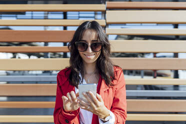 Lächelnde weibliche Fachkraft mit Sonnenbrille schreibt eine SMS, während sie an einer Holzwand steht - JRVF00328