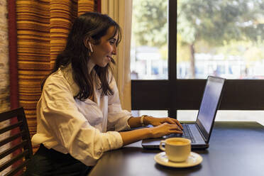 Lächelnde Unternehmerin, die einen Laptop benutzt, während sie in einem Café sitzt - JRVF00332