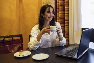 Glückliche junge Geschäftsfrau, die mit einer Tasse Kaffee in der Hand in ein Café schaut - JRVF00333