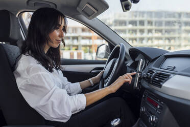 Junge Frau, die im Auto sitzend ein globales Positionierungssystem über ihr Smartphone einrichtet - JRVF00341