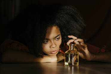 Young woman looking at bottle while lying on floor at home - TCEF01595