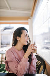 Beautiful woman with cup looking through window in coffee shop - GRCF00690
