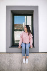 Beautiful woman looking away while sitting on window sill - GRCF00700