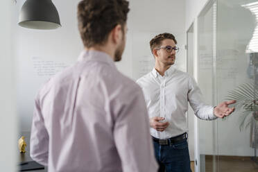 Businessman explaining male colleague in office - DIGF14683