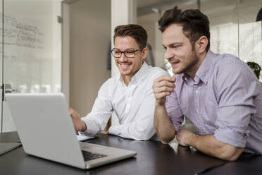 Männlicher Unternehmer arbeitet mit einem Kollegen im Büro am Laptop - DIGF14700