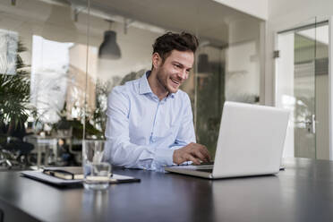 Lächelnder Geschäftsmann mit Laptop am Schreibtisch im Büro - DIGF14703
