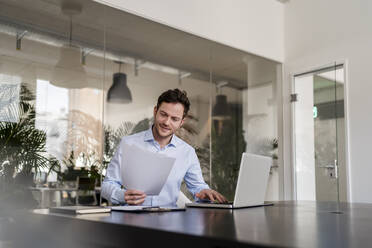 Geschäftsmann mit Dokument, der im Büro am Laptop arbeitet - DIGF14712