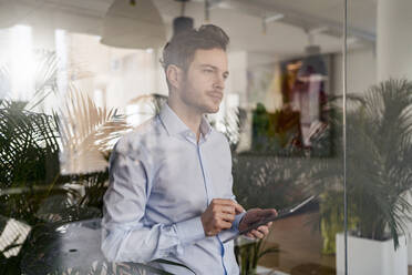 Geschäftsmann mit digitalem Tablet durch Glas im Büro gesehen - DIGF14722