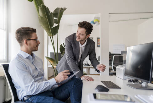 Geschäftsmann im Gespräch mit einem männlichen Kollegen am Schreibtisch im Büro - DIGF14735