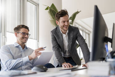 Lächelnde Geschäftsleute diskutieren über Computer am Schreibtisch im Büro - DIGF14736