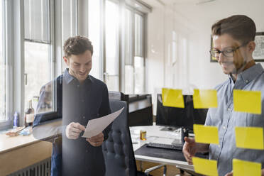 Männliche Kollegen, die durch Glasscheiben gesehen werden, während sie im Büro diskutieren - DIGF14737