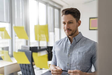 Confident businessman brainstorming while looking at adhesive notes at office - DIGF14742