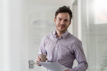 Male entrepreneur with disposable cup and document at office - DIGF14755