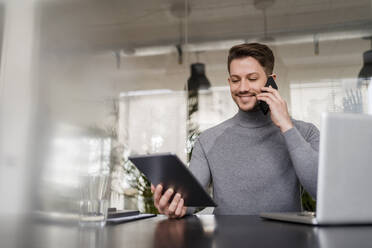 Male entrepreneur talking on smart phone while holding digital tablet in office - DIGF14758