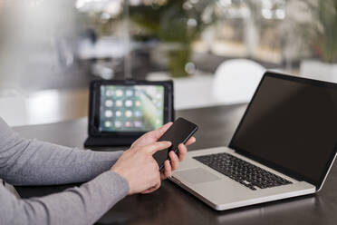 Businessman's hands using smart phone by laptop at office - DIGF14783