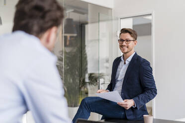 Male entrepreneur smiling while discussing with colleague in office - DIGF14787