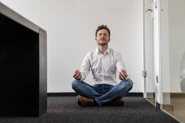 Männlicher Unternehmer meditiert Yoga im Büro an der Wand - DIGF14789