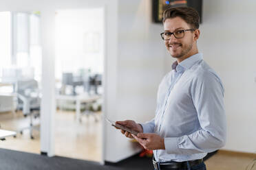 Lächelnder männlicher Unternehmer mit digitalem Tablet im Büro stehend - DIGF14798