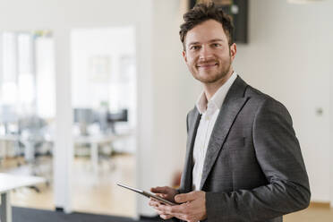 Lächelnder gut aussehender Geschäftsmann mit digitalem Tablet im Büro - DIGF14806