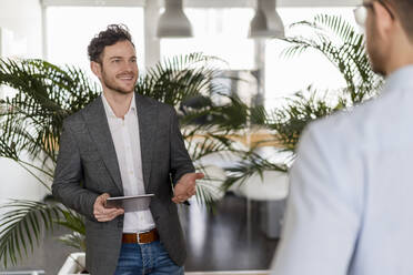 Smiling businessman with digital tablet discussing with male colleague at office - DIGF14807