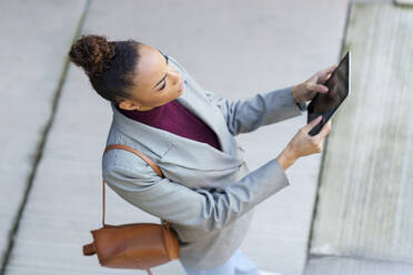 Unternehmerin mit Tasche, die ein digitales Tablet benutzt, während sie auf dem Fußweg steht - JSMF01980